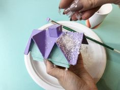 a person is painting some purple and green things on a plate with paintbrushes