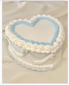 a white and blue heart shaped cake sitting on top of a table next to a pillow