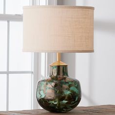 a green glass vase sitting on top of a wooden table next to a white lamp