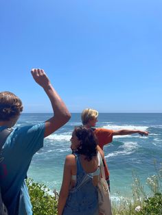 some people are standing by the ocean and pointing at something in the air with their hands