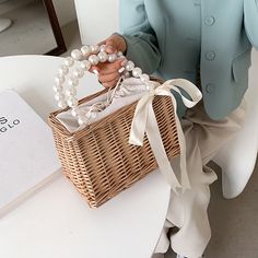 a woman sitting on a chair holding a wicker basket with white pearls in it