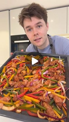 a man holding up a pan filled with chicken and peppers