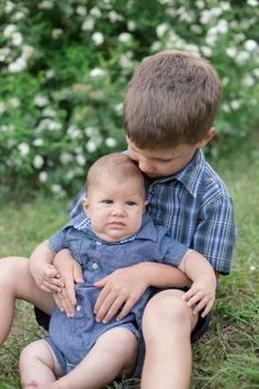 two young boys sitting in the grass with their arms around each other