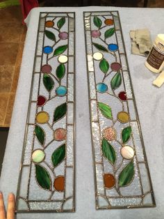 two stained glass windows sitting on top of a table next to a person's hand