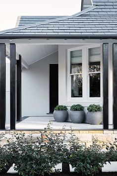 a white house with black shutters and two planters on the front porch area