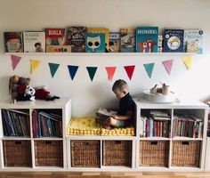 a young boy sitting on top of a bookshelf next to baskets filled with books