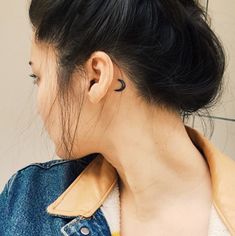 a woman with a tattoo on her left ear wearing a blue jacket and white shirt