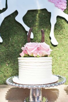 a white cake with pink flowers on top sitting in front of a metal horse sculpture