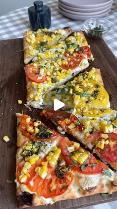 several slices of pizza with tomatoes, corn and cheese on a cutting board next to plates