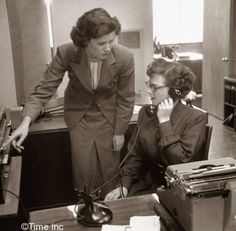 two women are talking on telephones in an office