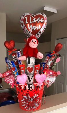 a valentine's day arrangement in a basket with balloons, candy and heart shaped balloons