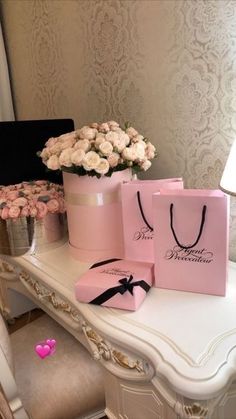 two pink bags sitting on top of a white table next to flowers and a vase