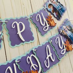 some purple and blue paper signs hanging on a white wooden wall with fall leaves in front of them