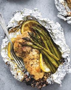 chicken and asparagus wrapped in foil with lemon wedges on the side, ready to be served