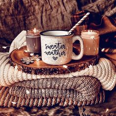 two coffee mugs sitting on top of sweaters with candles in front of them