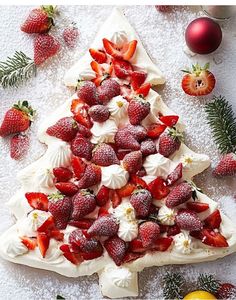 a christmas tree shaped cake with strawberries on top and other decorations around it in the background