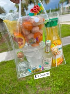 a person holding a clear plastic bag filled with fruit and drinks on the side of a road