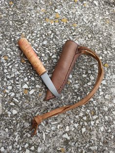 a knife that is laying on the ground next to a leather case with a wooden handle