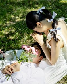 two people laying on the ground with flowers in their hands and one person holding a flower