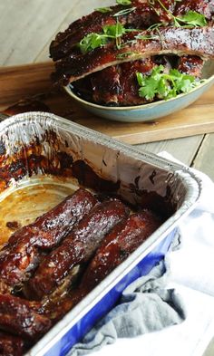 ribs in tin foil sitting on top of a cutting board next to a bowl of greens