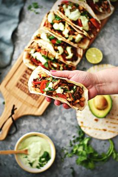 a person holding a taco in front of some tortillas and guacamole