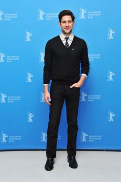 a man standing in front of a blue wall wearing a black sweater and tie with his hands in his pockets