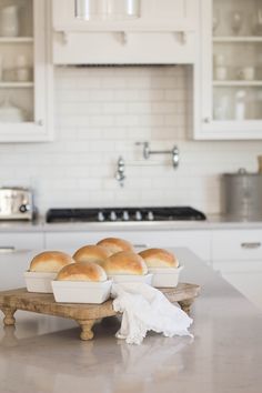 rolls are sitting on a wooden tray in the middle of a kitchen counter with white cabinets