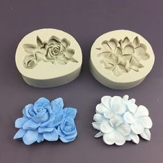 four flower molds sitting on top of a table next to each other, one has a blue rose and the other is white