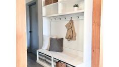 a white bench with two coats hanging on it's back and some baskets underneath