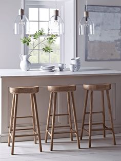 three wooden stools sit in front of a white counter with two vases on it