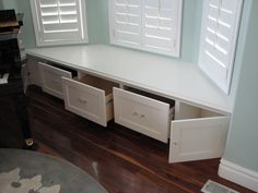 a white bench with drawers in front of two windows and a piano on the other side