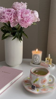 pink flowers are in a vase next to a cup and saucer