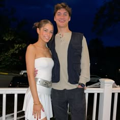 a young man and woman posing for a photo on a porch at night with their arms around each other