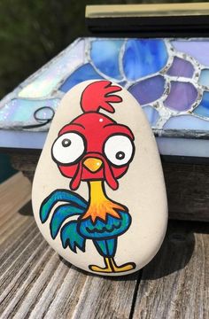 a painted rock sitting on top of a wooden table next to a stained glass window