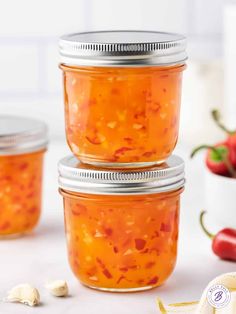 three jars filled with food sitting on top of a white counter next to garlic and peppers