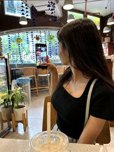 a woman sitting at a table with a cell phone in her hand and looking at the screen