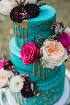 a three tiered cake with flowers and dripping icing on the top, sitting on a table