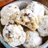 a bowl filled with cookies covered in powdered sugar on top of a wooden table