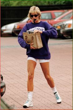 a woman is walking down the street in shorts and a sweatshirt with her handbag