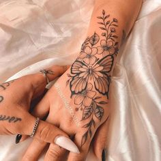 a woman's hand with tattoos and flowers on her left arm, sitting on a white sheet