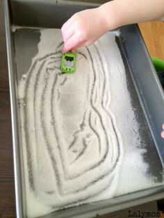 a child is playing with sand in a metal tray on the floor and holding a green toy car