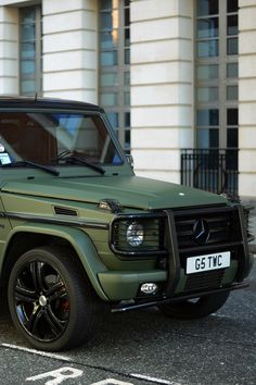 a green mercedes g - class is parked in front of a building