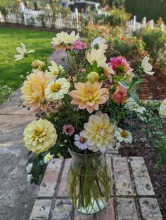 a vase filled with lots of flowers sitting on top of a wooden table next to a garden