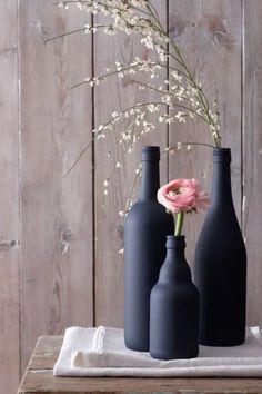 three black vases with flowers in them on a table