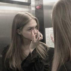 a woman standing in front of a mirror with her hand on her face and looking at the mirror