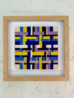 an art piece in a wooden frame with blue and yellow squares on the wall behind it