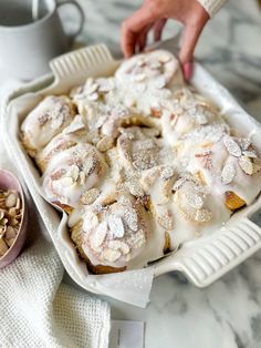 a person placing cinnamon rolls on top of a baking pan next to a bowl of nuts