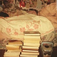 a pile of books sitting on top of a bed next to a phone and alarm clock