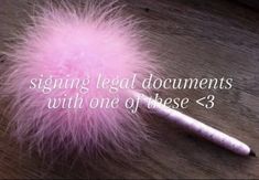 a pink feather ball sitting on top of a wooden table next to a white pen