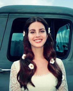 a woman standing in front of a green truck with flowers on her hair and smiling at the camera